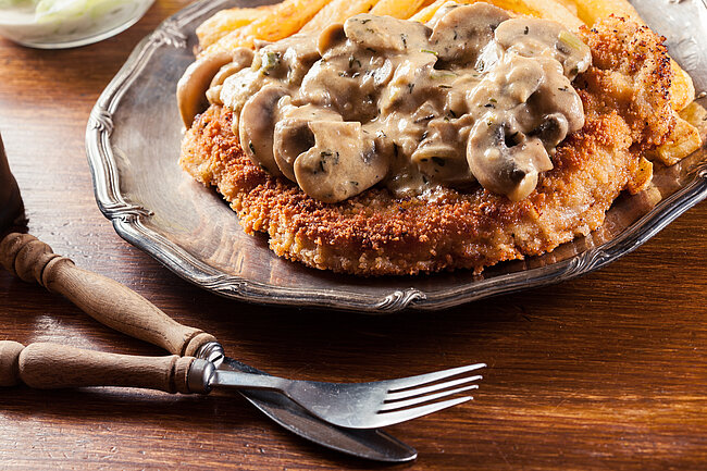 Panierte Schnitzel mit goldbrauner Panade, bedeckt mit einer cremigen Champignon-Sahnesauce, serviert auf einem Teller.