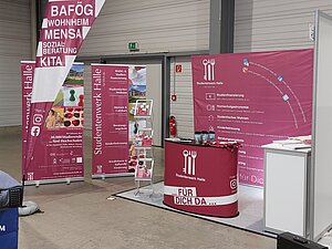 Ein Messe- oder Informationsstand mit Plakaten und Flyern zu Themen wie BAföG, Wohnen, Mensa und Kita. Der Stand ist mit einem roten Tisch und Informationsmaterial ausgestattet. Die Veranstaltung findet am 22. Februar 2024 statt.