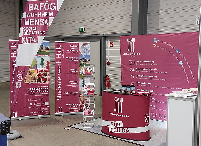 Ein Messe- oder Informationsstand mit Plakaten und Flyern zu Themen wie BAföG, Wohnen, Mensa und Kita. Der Stand ist mit einem roten Tisch und Informationsmaterial ausgestattet. Die Veranstaltung findet am 22. Februar 2024 statt.