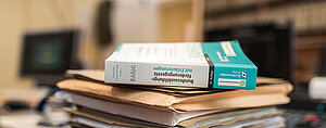 BAföG Buch; Foto: DSW/Jan Eric Euler Ein Stapel Bücher und Papiere auf einem Tisch. Obenauf liegen zwei Bücher, eines mit weißem und eines mit blauem Einband. Die Bücher scheinen sich mit rechtlichen oder behördlichen Themen zu befassen, wie die Titel vermuten lassen.