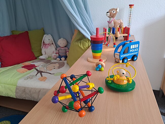 Spielzeug auf einem Tisch: bunte Kugelkonstruktion aus buntem Holz, Spielzeugpolizeiwagen aus Holz, bunte Holzklötze und ein Stofftierhund.