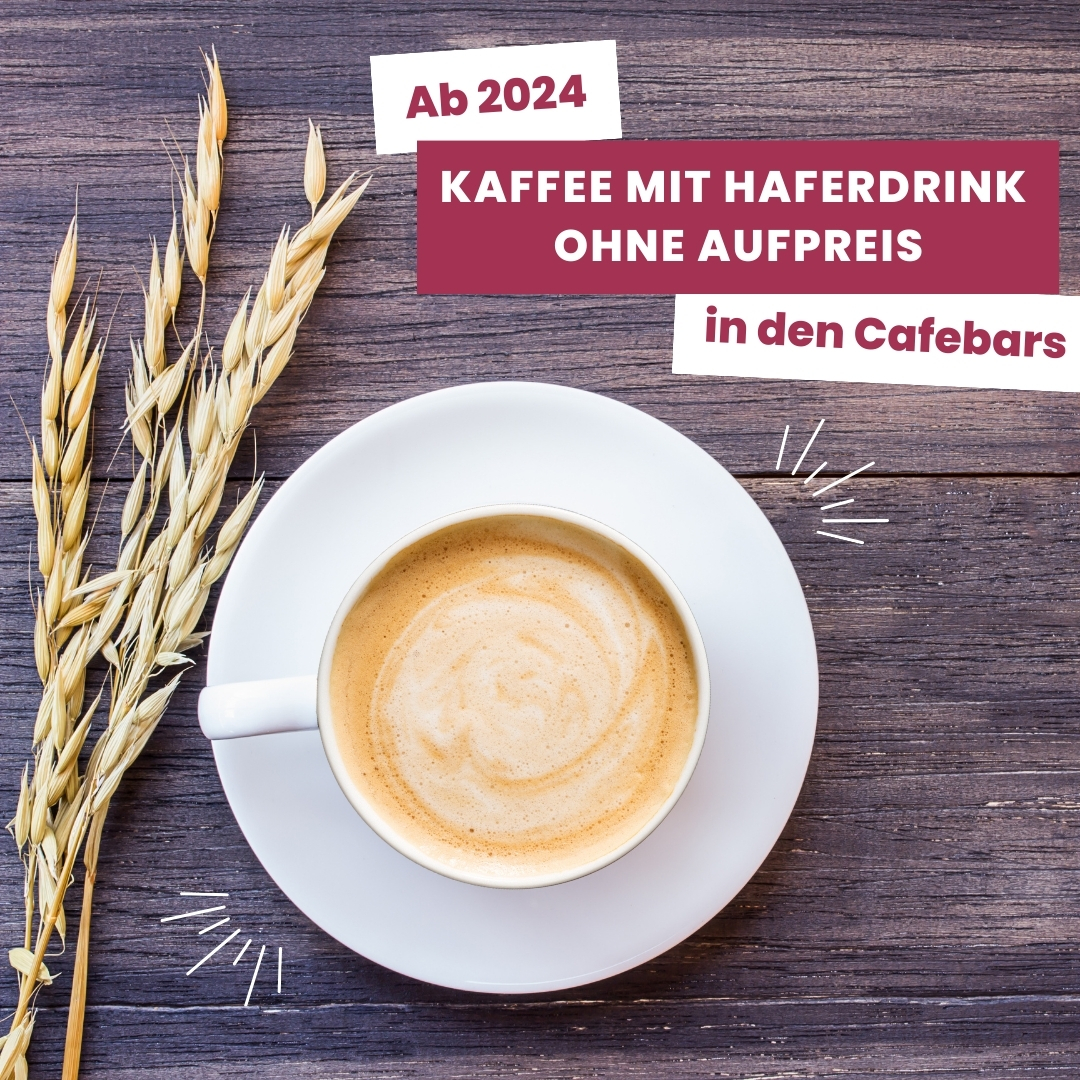 "Ab 2024: Kaffee mit Haferdrink ohne Aufpreis in den Cafebars. Ein Bild zeigt eine Tasse Kaffee mit Hafermilchschaum und Haferhalmen daneben auf einem Holztisch."