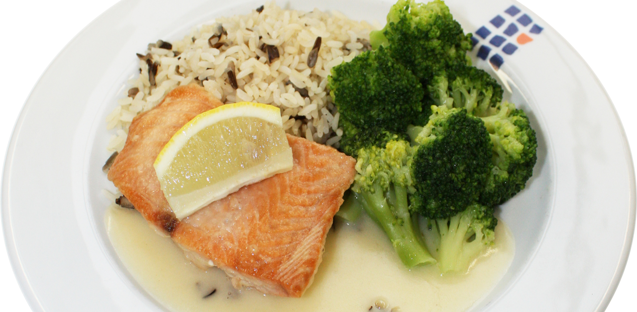 Ein Teller mit Lachsfilet, garniert mit Zitronenscheiben, dazu Brokkoli und brauner Reis. Der Lachs ist in einer hellen Sauce serviert.