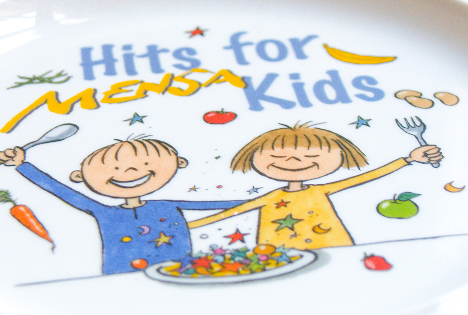 "Ein weißer Teller mit der Aufschrift 'Hits for Kids' zeigt zwei lachende Kinder, die Besteck in die Höhe halten. Um sie herum sind verschiedene Lebensmittel wie Karotten, Äpfel und Nudeln dargestellt. Der Text 'Menü' ist kreativ in die Szene integriert."